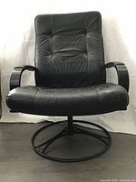 Front view of black leather swivel chair with padded tufted seat and backrest, curved arms, and circular metal base.