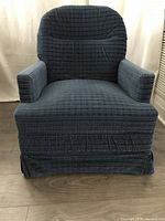 Front view of the blue fabric swivel chair showing padded seat, back, and armrests with pleated skirt base.