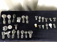 Overview of all 29 glass bottle and wine stoppers laid out on dark fabric, showing different sizes and shapes.