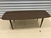 Front view of narrow brown coffee table with wood grain top and tapered legs.