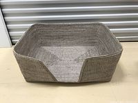 Photo of a light brown woven dog bed with open front side, rectangular shape and raised edges on other sides.