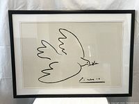 Framed black and white peace dove art print behind glass with signature resembling Picasso style.