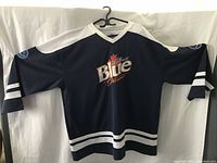 Front view of blue Labatt Blue Pilsner hockey jersey with white shoulder panels, white stripes on arms and waist, embroidered Labatt Blue Pilsner logo in chest center.