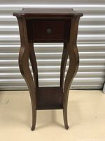 Front view of wooden plant stand with small drawer and curved legs, showing overall condition and design.