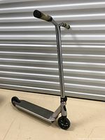 Full view of the silver kids scooter showing the T-bar handle with black rubber grips, and the black front and rear wheels.