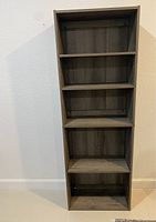 Front view of a tall wooden bookshelf with five shelves against a white wall.