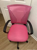Front view of the pink mesh office chair with black armrests and caster wheels on light wooden floor.