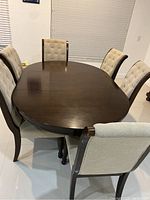 Photo showing oval dark wood dining table with six upholstered chairs around it.