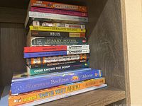 Stack of children's books with visible titles including classic literature and educational guides, neatly arranged on shelf.