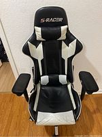 Front view of black and white S-Racer gaming chair, damaged leather on seat visible, padded headrest and lumbar support.
