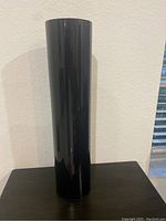 Full view of the tall black glass vase standing upright on a flat surface against a neutral background.