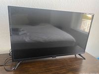 Black 30-inch Insignia flat screen television sitting on wooden surface, viewed from front with screen turned off.
