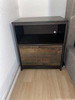Front view of one wooden night stand showing open shelf space and single drawer with rustic wood drawer front.