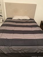 Full view of the queen size bed with padded headboard and mattress covered with striped comforter
