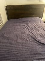 Photo of queen size bed with wooden headboard and mattress covered in purple bedding