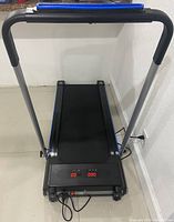 Top front view of electric Redliro treadmill showing black belt, digital display with red LED, collapsible handlebar with foam grips, plugged into power socket.
