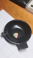 1.67ct pear-shaped opal cabochon placed in a black container showing bright play of color.