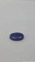 Oval cabochon shape, natural lapis lazuli in deep blue with natural inclusions and visible patterns on polished surface.