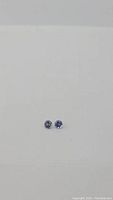 Two round, purple-blue diamond cut tanzanite stones on white background