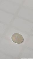 Oval cabochon Ethiopian opal gemstone on white background showing its play of color.