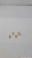 Four small oval cabochon stones of natural golden rutilated quartz with visible inclusions against white background.