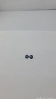 Pair of small oval cabochon cut blue pietersite stones seen side by side on white background, showing dark blue to gray patterns.