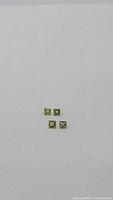 Four small square princess cut peridot gemstones arranged in a diamond shape on white background, showing green hues and clarity