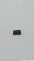 Single deep green baguette cut tourmaline gemstone on a plain background showing rectangular shape and color.