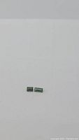 Two small natural green tourmaline baguette cut gemstones on plain white background, showing shape and color.
