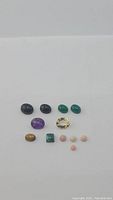 Photo showing assortment of polished and faceted natural gemstones arranged in groups on a white background.