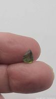 Photo of natural olive green sapphire held between fingers showing pear shape and color