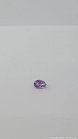 Close-up photo of a natural purple amethyst gemstone pear cut shape on white background.