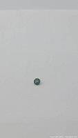Clear photo showing round cut teal blue sapphire against white background.