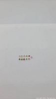 Image showing 12 small round cabochon cut stones in various rainbow colors arranged in two rows on a plain white background.
