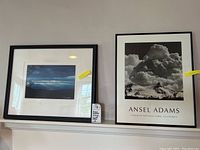 Two framed artworks on a shelf: left is color photo with signature, right is Ansel Adams Yosemite poster.