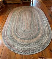 Full view of the oval braided rug on wooden floor with visible pattern and braided texture.