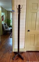 Full view of vintage wooden coat tree standing against wall near door with a four-legged base.