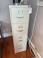 Front view of beige HON metal filing cabinet showing four drawers with handles and label holders, key inserted in top drawer lock.