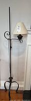 Full view of black metal floor lamp with beige fabric shade, showing scroll design and three-legged base.