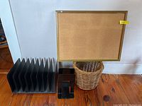 Photo showing the SteelMaster paper sorter, metal book ends, cork board with gold frame, and woven waste basket against a white wall on wood floor.