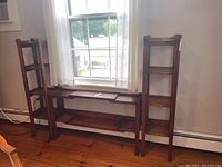 Front view of three-piece wooden shelving unit positioned in front of a window showing overall design and finish.