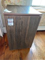 Front view of the Excellence mini refrigerator showing the wood grain laminated door and the brand/model metal badge.