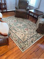 Full view of the Bob Mackie Home area rug laid out on wood floor with surrounding furniture showing the floral design and edge wear.