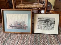 Two framed prints side by side on carpeted floor, one in color with light blue mat and one black and white with white mat