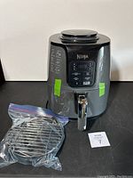 Full view of Ninja air fryer with display and front handle alongside packaged metal cooking rack.