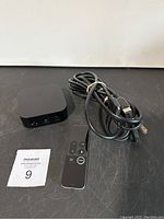 Apple TV device, remote control and HDMI cable laid out on table.