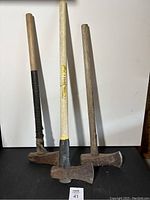 Full view of three axes with different wooden handles and rusted metal heads on a white background.