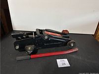 Side view of the floor car jack showing the entire jack and detached handle on black surface.