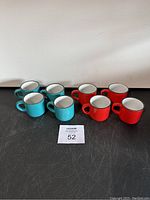 Eight ceramic espresso cups arranged in two groups by color, four turquoise and four red cups.