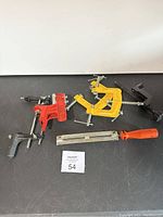 Set of three clamps and an orange-handled file laid out on a black surface with a lot number below.